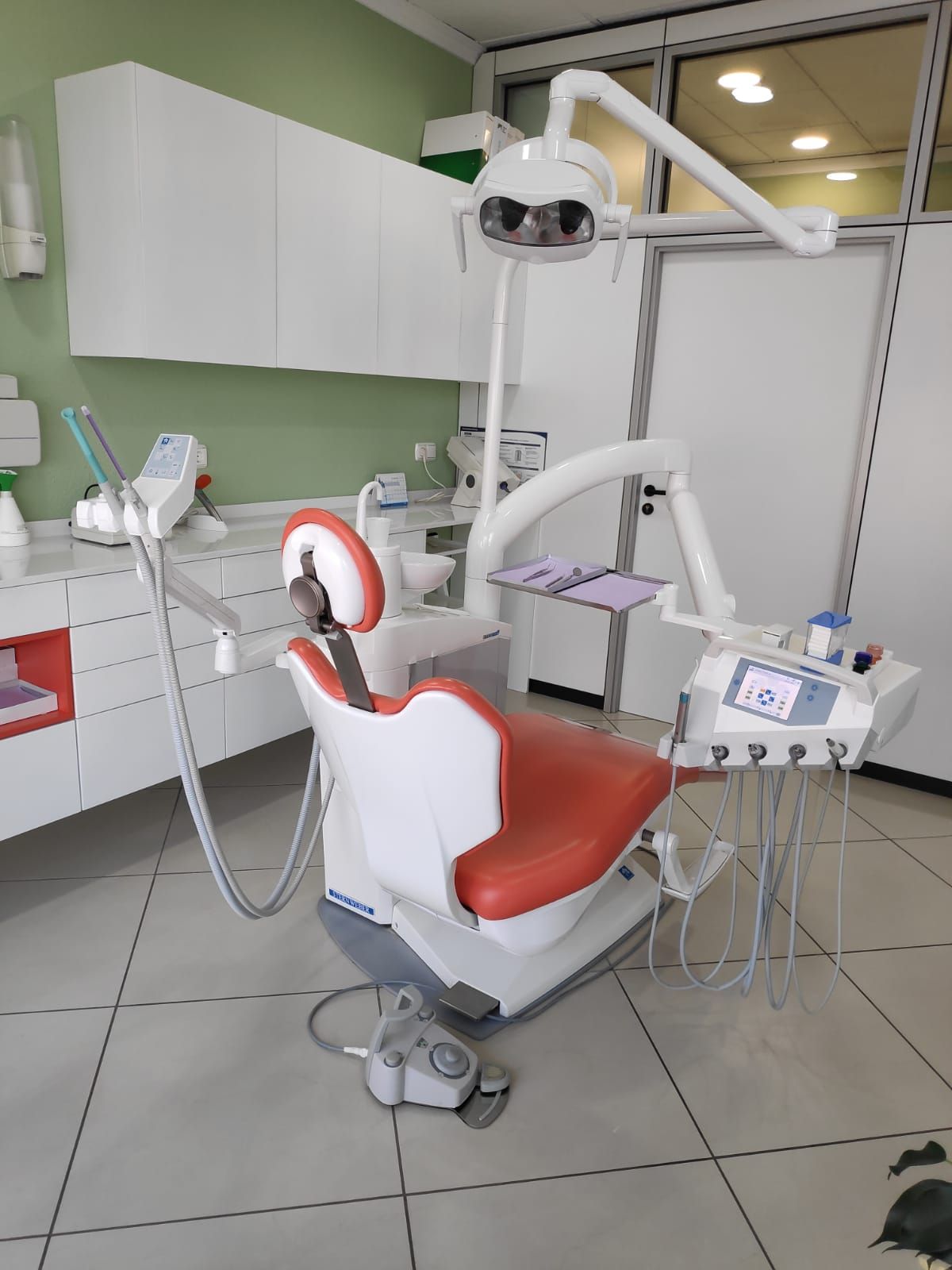 Gabinete dental con sillón naranja, mobiliario blanco y luz natural